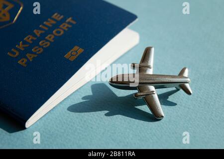 Passeport étranger ukrainien avec figurine métallique de petit avion sur fond bleu clair ensoleillé. Photo conceptuelle tendance de voyage et d'aviation Banque D'Images