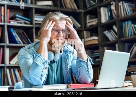 Jeune homme fatigué stressé dans des verres avec une tête de massage des yeux fermés. Banque D'Images