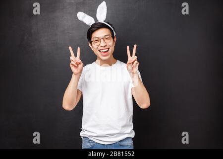 Vacances, fête et concept de Pâques. Joyeux gars asiatique mignon dans les oreilles et les verres de lapin montrant des signes de paix, semble kawaii célébrant la journée orthodoxe sur Banque D'Images