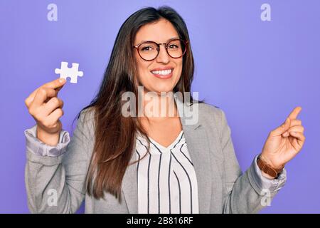 La jeune femme d'affaires hispanique qui tient le puzzle de la paix comme la coopération et l'Union sur le travail très heureux pointant avec la main et le doigt sur le côté Banque D'Images