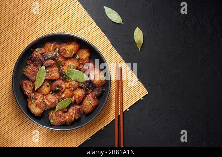 Adoro porc dans un bol noir sur fond d'ardoise sombre. L'adobo de porc ou l'Adobong Baboy est un plat de cuisine philippine au ventre de porc braisé, aux feuilles de laurier, à la sauce soya Banque D'Images