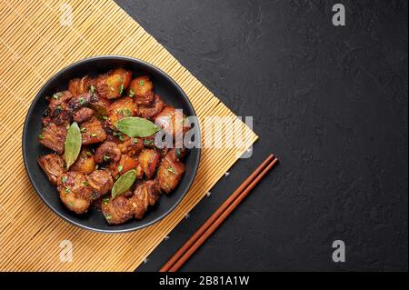 Adoro porc dans un bol noir sur fond d'ardoise sombre. L'adobo de porc ou l'Adobong Baboy est un plat de cuisine philippine au ventre de porc braisé, aux feuilles de laurier, à la sauce soya Banque D'Images