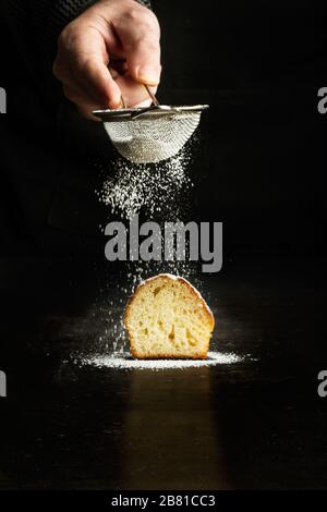 Homme saupoudrer de sucre en poudre sur un cupcake sur fond sombre Banque D'Images