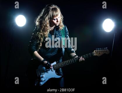 Guitariste fille avec guitare noire et blanche. Derrière deux projecteurs. L'arrière-plan est noir Banque D'Images