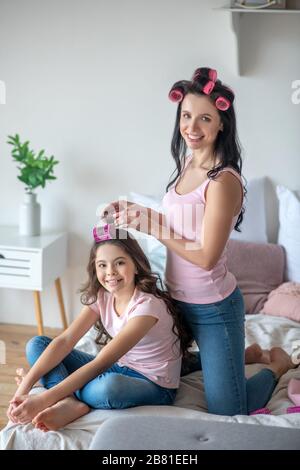 Maman avec des fers à friser les cheveux à sa fille Banque D'Images