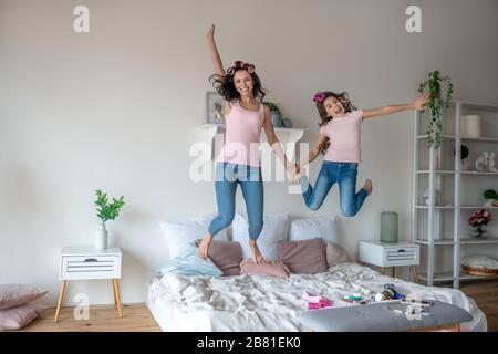 Maman et fille avec des bigoudis sautant sur le lit Banque D'Images