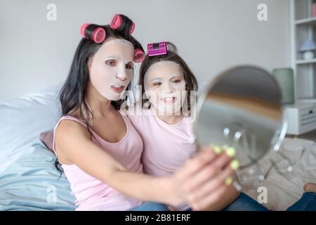 Maman et fille avec des bigoudis regardant dans le miroir Banque D'Images