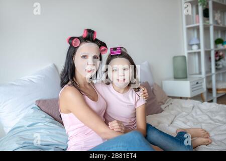 Maman et fille avec des bigoudis assis sur le lit Banque D'Images