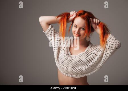 Vue avant de la belle jeune femme qui s'amuse et qui tient les cheveux avec les mains. Jolie dame aux cheveux rouges regardant l'appareil photo et souriante. Concept de beaut Banque D'Images