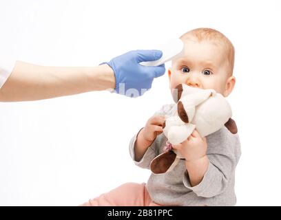 Le pédiatre ou l'infirmière vérifie la température corporelle du bébé garçon à l'aide d'un thermomètre frontal infrarouge (pistolet thermomètre) pour les symptômes de maladie Banque D'Images