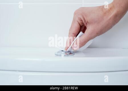 gros plan d'un homme caucasien en appuyant sur le bouton de rinçage d'une toilette couvrant ses doigts avec un morceau de papier toilette Banque D'Images