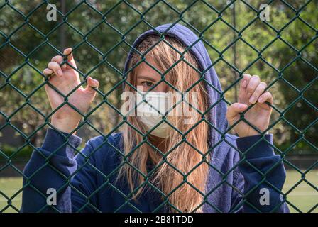 Bordure fermée. Quarantaine. Une jeune femme portant un masque de protection se trouve derrière la bordure de clôture. COVID-19 virus de la pandémie d'infection du coronavirus. Banque D'Images