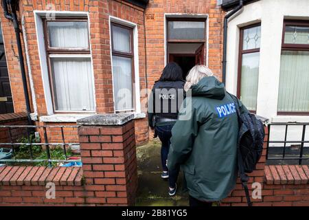 Les officiers du PSNI TSG entrent dans une propriété lors d'une recherche dans une rue mitoyenne au large de la route Crumlin dans la région de Shankill au nord de Belfast. La recherche faisait partie de l'opération Pangea qui vise la vente en ligne de médicaments et de dispositifs médicaux contrefaits et illicites. Banque D'Images