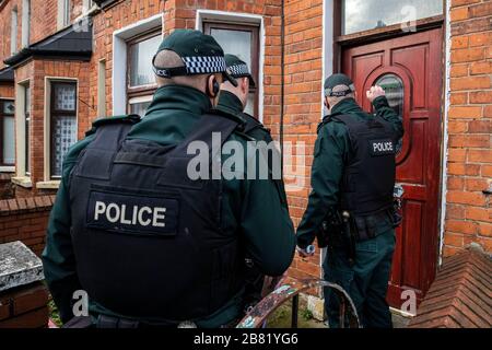 Les officiers du PSNI TSG entrent dans une propriété lors d'une recherche dans une rue mitoyenne au large de la route Crumlin dans la région de Shankill au nord de Belfast. La recherche faisait partie de l'opération Pangea qui vise la vente en ligne de médicaments et de dispositifs médicaux contrefaits et illicites. Banque D'Images