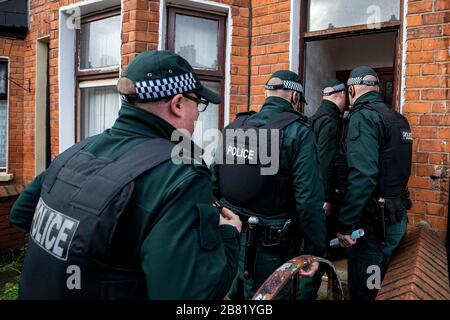 Les officiers du PSNI TSG entrent dans une propriété lors d'une recherche dans une rue mitoyenne au large de la route Crumlin dans la région de Shankill au nord de Belfast. La recherche faisait partie de l'opération Pangea qui vise la vente en ligne de médicaments et de dispositifs médicaux contrefaits et illicites. Banque D'Images