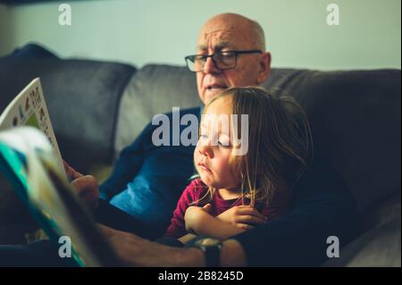 Un grand-père lit à son petit-enfant d'âge préscolaire sur le canapé à la maison Banque D'Images