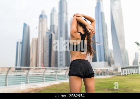 Jeune fille sportive portant des vêtements de sport roses qui s'étirent à proximité des gratte-ciel, se préparant à l'entraînement, à l'entraînement en extérieur, se réchauffant après ou avant la fi Banque D'Images