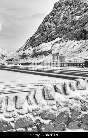 Conduisez sur la gauche dans différentes langues et les panneaux des attractions touristiques sur la route dans Glencoe couvert de neige, Highlands, Ecosse en hiver - noir et blanc Banque D'Images