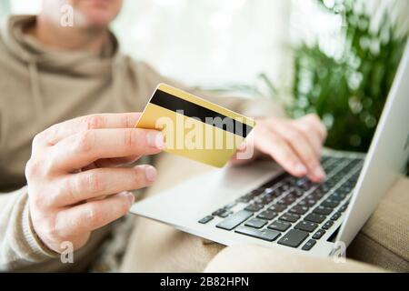 Un homme adulte heureux assis à la maison sur un canapé avec ordinateur portable et carte de crédit. Payer des factures et des commandes. Concept de commerce électronique et d'achat en ligne. Banque D'Images