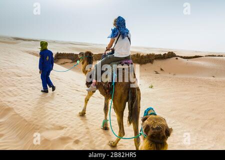 Guide de femme et de tuareg dans une promenade dromadaire dans le désert. Banque D'Images