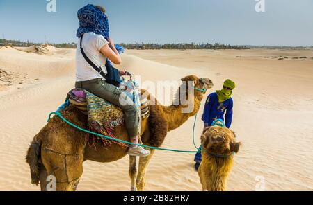 Guide de femme et de tuareg dans une promenade dromadaire dans le désert. Banque D'Images