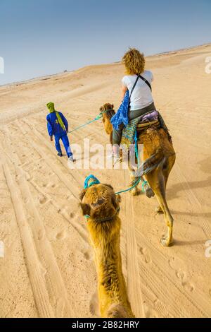 Guide de femme et de tuareg dans une promenade dromadaire dans le désert. Banque D'Images