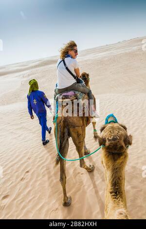 Guide de femme et de tuareg dans une promenade dromadaire dans le désert. Banque D'Images