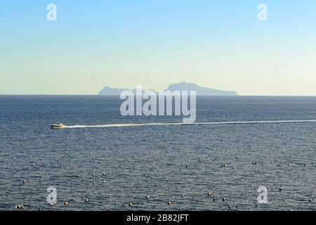 L'île de Capri sur la ligne d'horizon au-dessus du golfe de Naples vue du front de mer de la ville dans une vue sur le paysage au coucher du soleil avec un petit bateau lentement n Banque D'Images