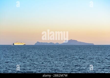 L'île de Capri sur la ligne d'horizon au-dessus du golfe de Naples vue du front de mer de la ville dans une vue sur le paysage au coucher du soleil avec un grand bateau lentement navi Banque D'Images