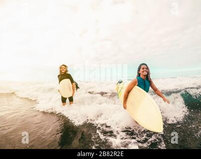 Les surfeurs se coulent ensemble avec des planches de surf sur l'océan au coucher du soleil - Sporty fit des amis qui s'amusent à surfer sur les hautes vagues