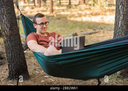 Concept d'internet ou d'ordinateur portable tout en camping en lieu éloigné, ordinateur portable gris en hamac Banque D'Images