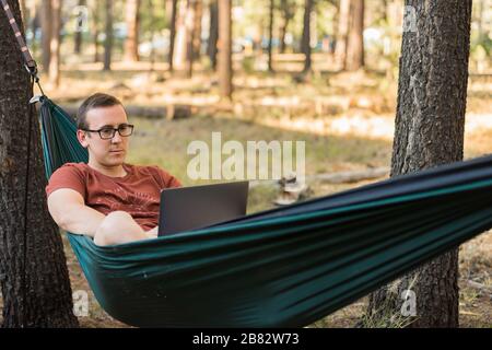 Concept d'internet ou d'ordinateur portable tout en camping en lieu éloigné, ordinateur portable gris en hamac Banque D'Images