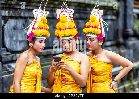 Jeunes filles hindoues balinaises regardant UN téléphone mobile (Cellphone) à la cérémonie Batara Turun Kabeh, Temple Besakih, Bali, Indonésie. Banque D'Images