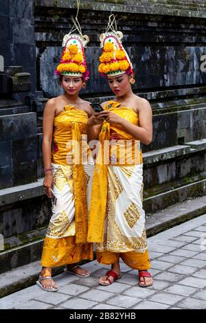 Deux jeunes filles hindoues balinaises regardant UN téléphone mobile (téléphone portable) à la cérémonie Batara Turun Kabeh, Temple de Besakih, Bali, Indonésie. Banque D'Images