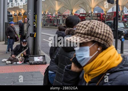 Stratford, Londres, Royaume-Uni. 19 mars 2020. Un homme est assis sur un pavé et joue sur le saxophone tandis que d'autres se trouvent dans le centre commercial Stratford. Les gens pressés d'acheter les autres articles autour du centre commercial Stratford en raison de la propagation du coronavirus. Crédit: Marcin Nowak/Alay Live News Banque D'Images