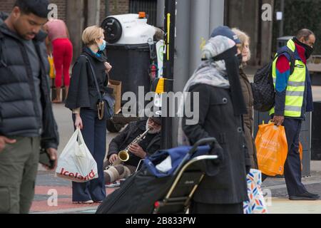 Stratford, Londres, Royaume-Uni. 19 mars 2020. Un homme est assis sur un pavé et joue sur le saxophone tandis que d'autres se trouvent dans le centre commercial Stratford. Les gens pressés d'acheter les autres articles autour du centre commercial Stratford en raison de la propagation du coronavirus. Crédit: Marcin Nowak/Alay Live News Banque D'Images