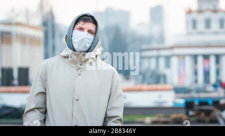 Portrait gros plan jeune européen homme dans un masque médical jetable de protection marchant à l'extérieur. Nouveau coronavirus (COVID-19). Concept de soins de santé Banque D'Images