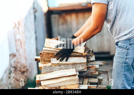 Un tas de bois de chauffage empilé, préparé pour chauffer la maison. Collecte de bois de feu pour l'hiver ou le feu de joie. L'homme tient le bois de feu dans les mains Banque D'Images