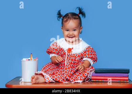 Jolie fille allemande de race mixte d'un an d'Asie caucasienne portant une robe rouge souriant regardant gentiment l'appareil photo sur fond bleu Banque D'Images