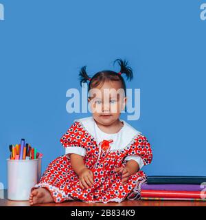 Jolie fille allemande de race mixte d'un an d'Asie caucasienne portant une robe rouge souriant regardant gentiment l'appareil photo sur fond bleu Banque D'Images