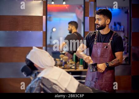 Maître coupe les cheveux et la barbe des hommes dans le barbershop, coiffeur fait la coiffure pour un jeune homme. Travailler dans le salon de coiffure, le processus des cheveux Banque D'Images