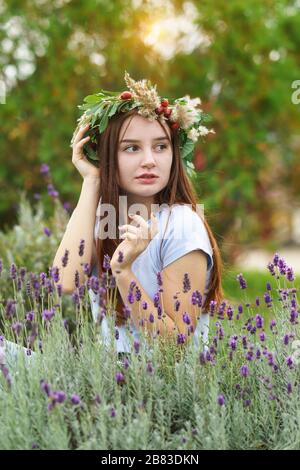 Belle fille à poil long dans une couronne de fleurs et de baies. Portrait sur fond lavande Banque D'Images