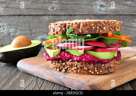 Superfood sandwich avec houmous de betterave, d'avocat, les légumes et les verts, sur pain de grains entiers contre un fond de bois Banque D'Images