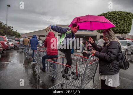 Tijuana, Mexique. 18 mars 2020. Un enfant qui s'ennuyait pendant la longue attente a retiré ses bottes en caoutchouc et joue sur le chariot à provisions sous la pluie alors que beaucoup de gens font la queue et attendent de faire du shopping. Craignant la propagation du coronavirus, les Mexicains à la frontière avec les États-Unis vont faire des achats de hamster. Jusqu'à présent, le Mexique a signalé 118 personnes infectées par le Covid-19. Les États-Unis ont presque 10 000 cas confirmés. Crédit: Omar Martínez/dpa/Alay Live News Banque D'Images