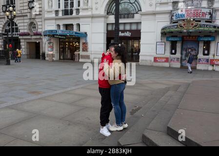 Alors que la pandémie de Coronavirus s'étend à travers le Royaume-Uni, les entreprises et les lieux de divertissement qui ne sont pas déjà fermés avec la menace de pertes d'emploi, ont du mal à rester ouverts avec des rumeurs croissantes sur un verrouillage et des restrictions de voyage autour de la capitale. Alors que les Londoniens commencent à travailler à domicile, en observant les conseils du gouvernement pour distancer les réseaux sociaux, le serveur brésilien Luis et sa petite amie au pair Paula d'Espagne, baiser et hug dans un Piccadilly Circus exceptionnellement calme, le 19 mars 2020, à Londres, en Angleterre. Banque D'Images
