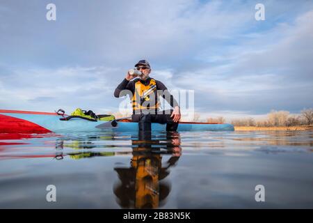 Le paddler masculin senior boit de l'eau pendant l'entraînement sur un stand up paddleboard, lac dans le Colorado, vue basse caméra d'action, loisirs, fitness Banque D'Images