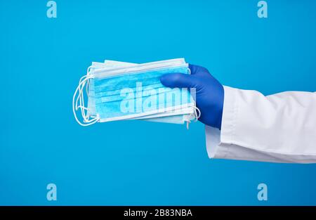 médecin en manteau blanc, les gants stériles en latex bleu contiennent des masques médicaux jetables en textile dans sa main sur un fond bleu Banque D'Images