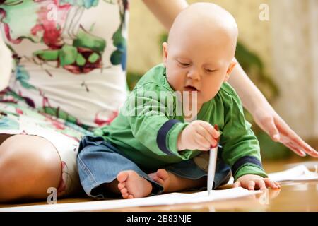 Petit garçon avec fille assise sur le sol et attire. Enfant en pull vert et en Jean bleu Banque D'Images