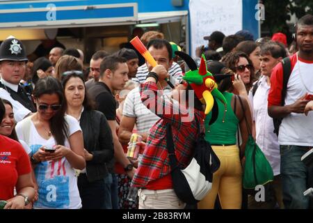 Jeune femme portant un chapeau de jester de cour et ayant un amusant souffle de corne multicolore au carnaval Notting Hill à Londres Banque D'Images