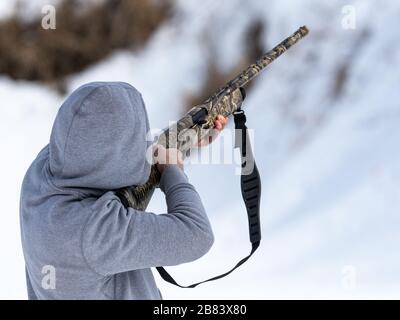 homme dans le tir à l'hoodie avec un fusil de chasse de camo Banque D'Images